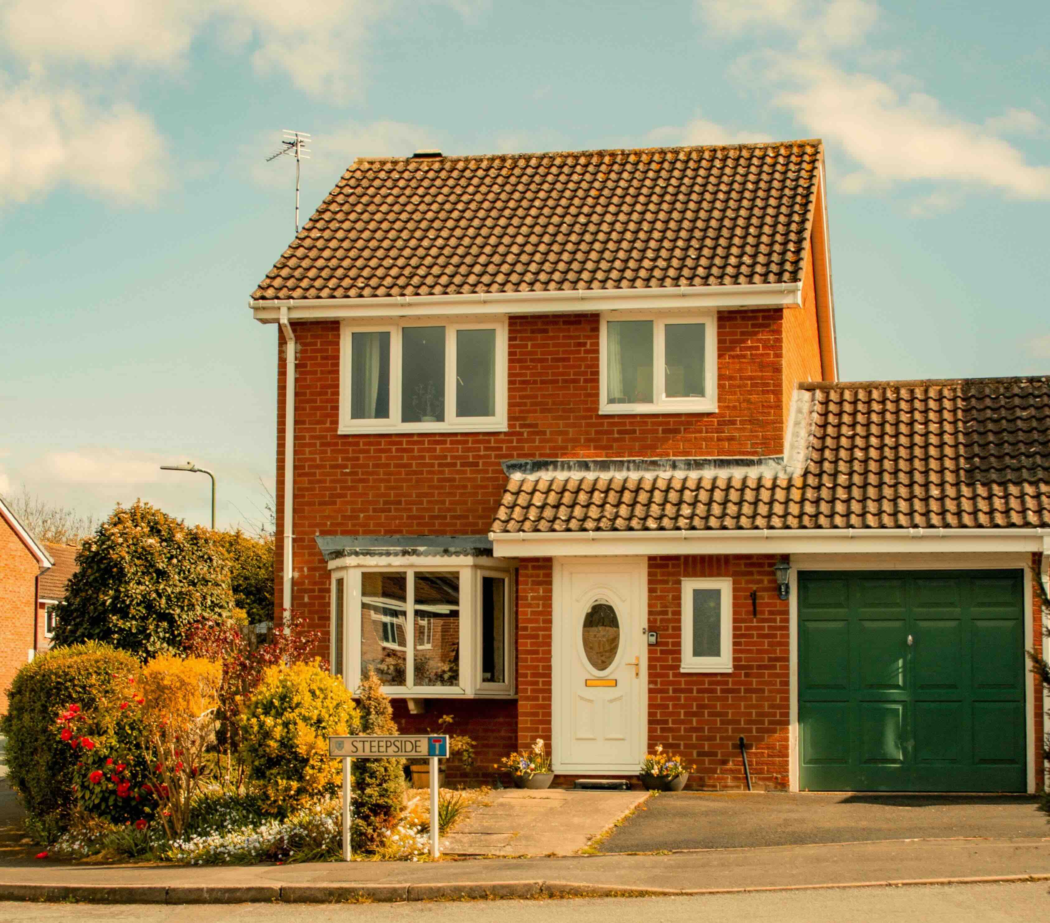 A typical British semi-detached home with red brick, bay window and a green garage door